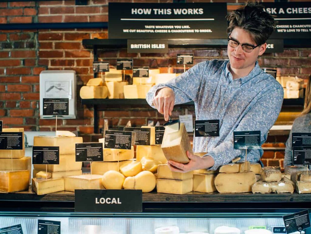 Cheese monger offering sample of local cheese to customer
