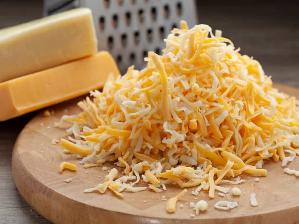 Grating a block of yellow and orange cheese