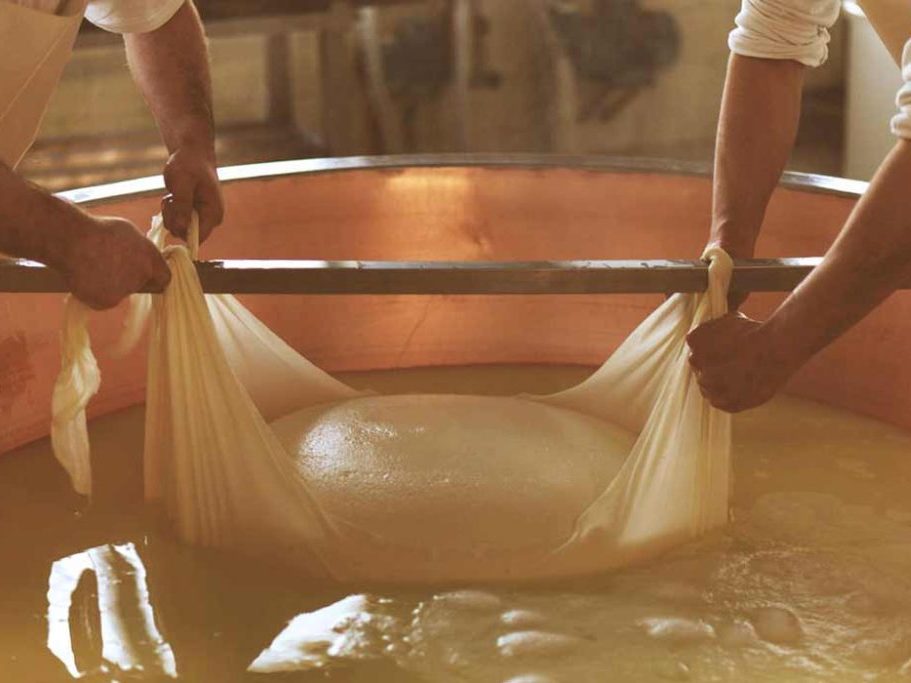Two cheesemakers lifting a mass of cheese curd from copper cauldron
