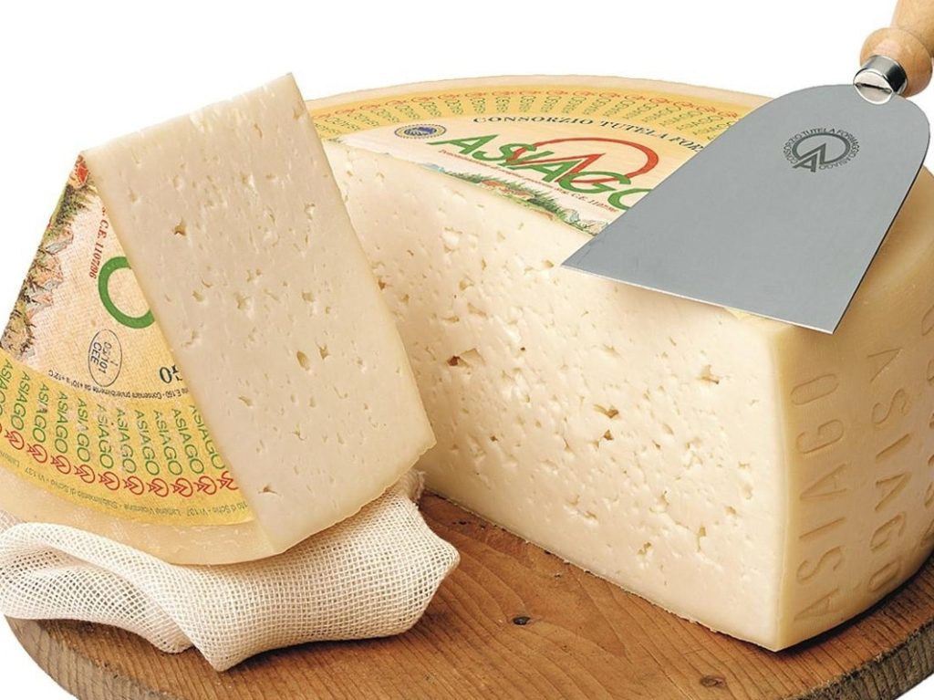 Hard wheel of Asiago cheese on wooden board