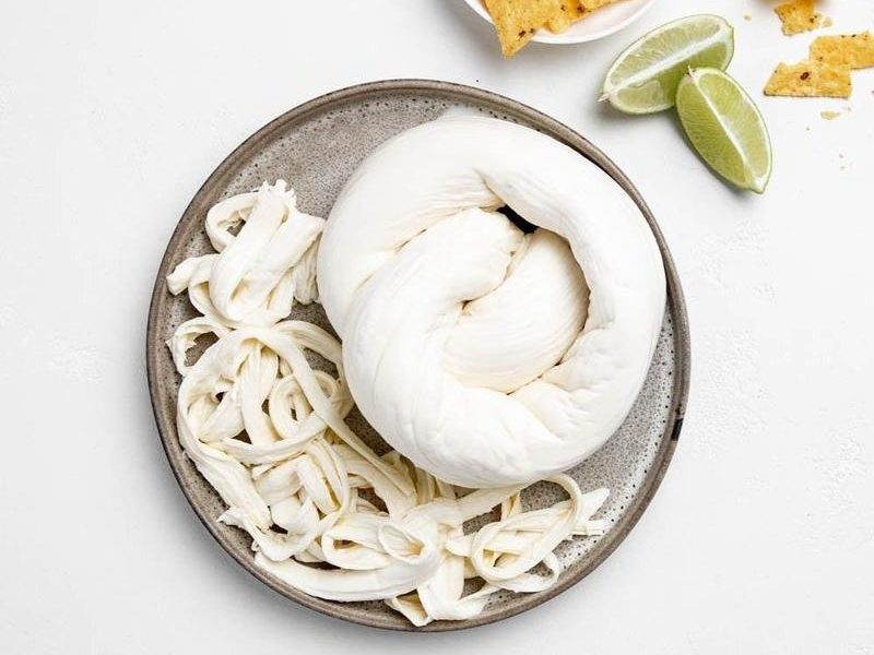 Stringy Oaxaca cheese on a plate with nachos and lime