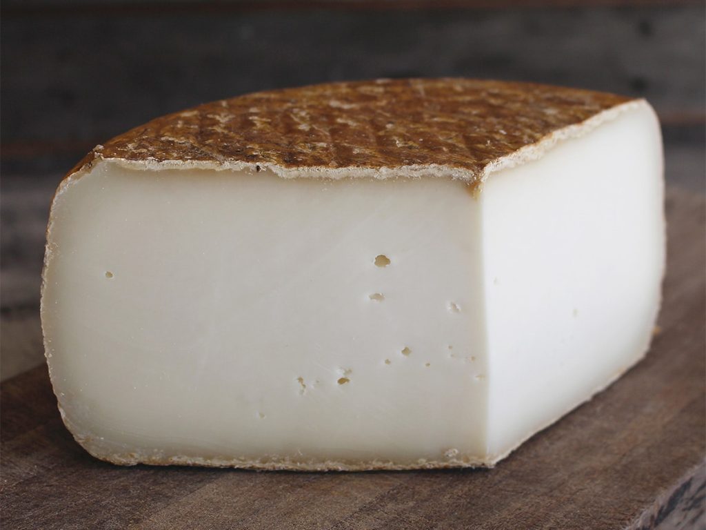 Lactose free Caprinelle Tomme de Chèvre hard cheese on a wooden table