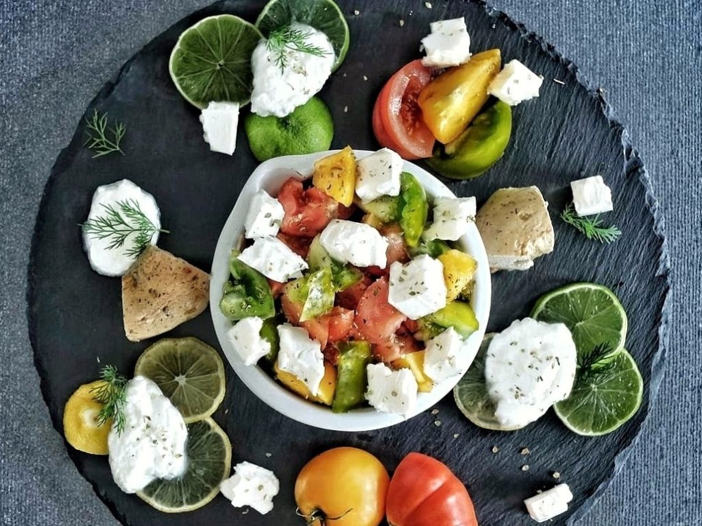 White bowl containing feta, heirloom tomatoes and sliced limes