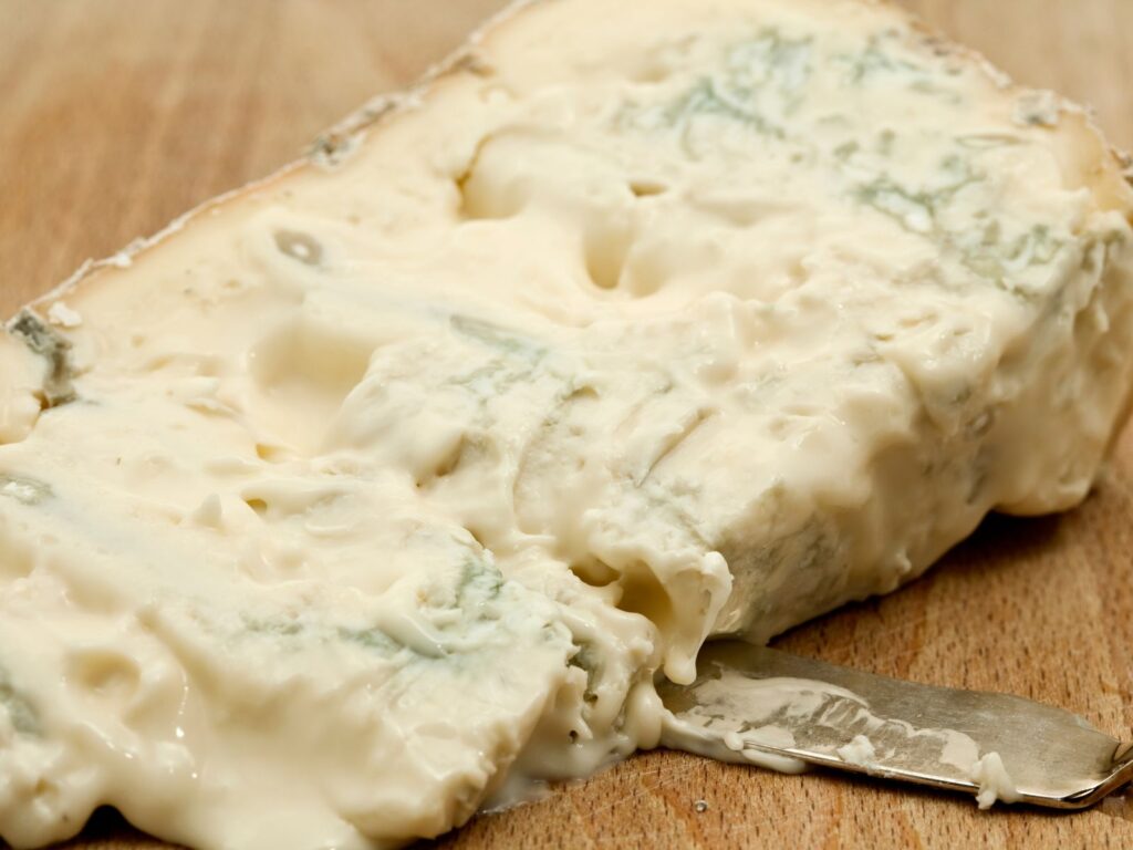 Oozy wedge of Italian Gorgonzola Dolce blue cheese on wooden board