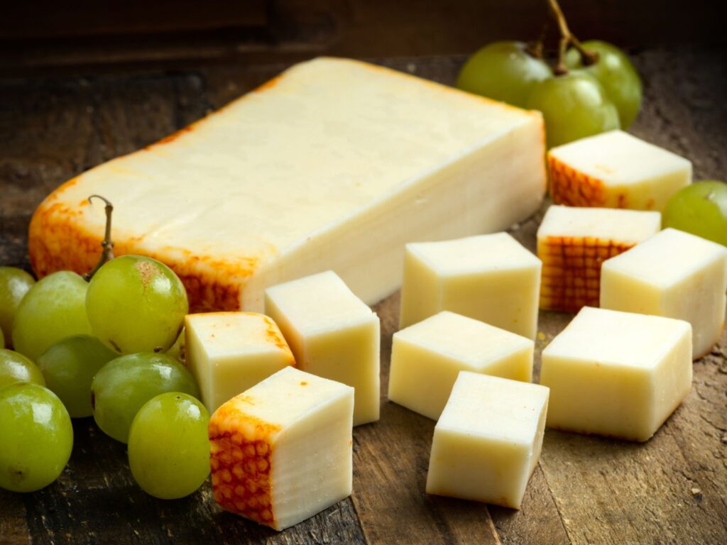 Soft Muenster cheese cut into cubes on a wooden cheese board with green grapes