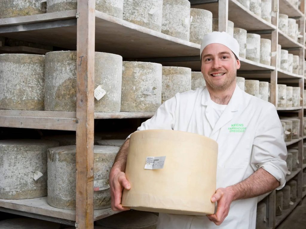 Male cheesemaker holding wheel of Keen's raw milk Cheddar