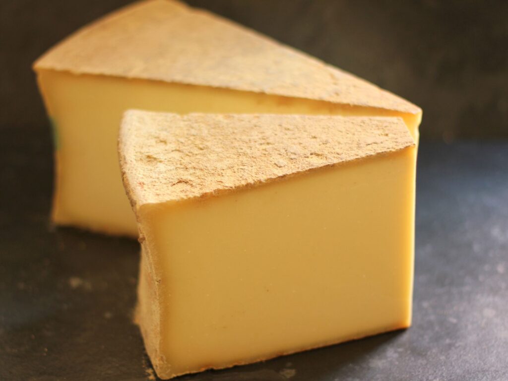 2 wedges of pressed hard cheese Beaufort on a wooden table