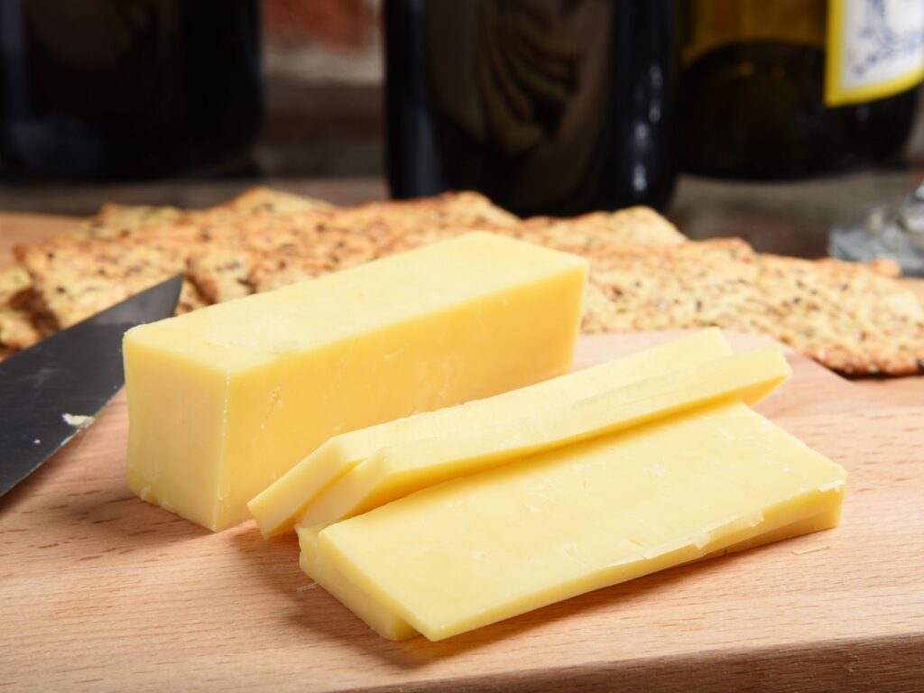Block of Cheddar cheese being sliced on wooden board