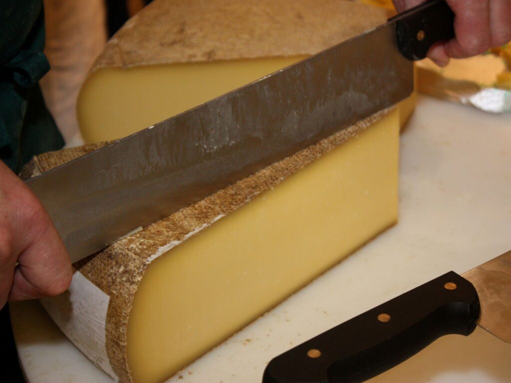 Wheel of Comté cheese being cut by cheese monger