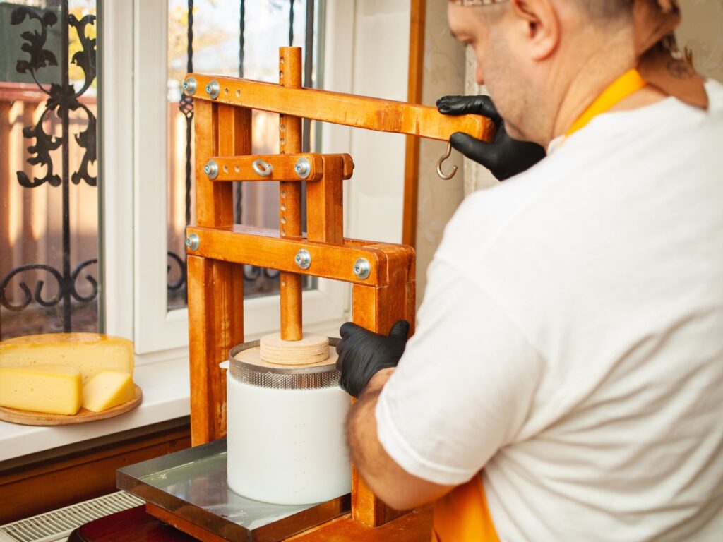 Home cheesemaker using wooden cheese press to make cheese