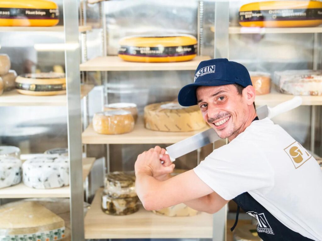 Cheesemonger Victor from K-SEIN Fromagerie holding cheese knife in front of cheese cabinet
