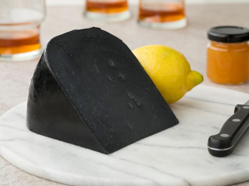 Wedge of Ruscello Black Lemon cheese on wooden board next to yellow lemon