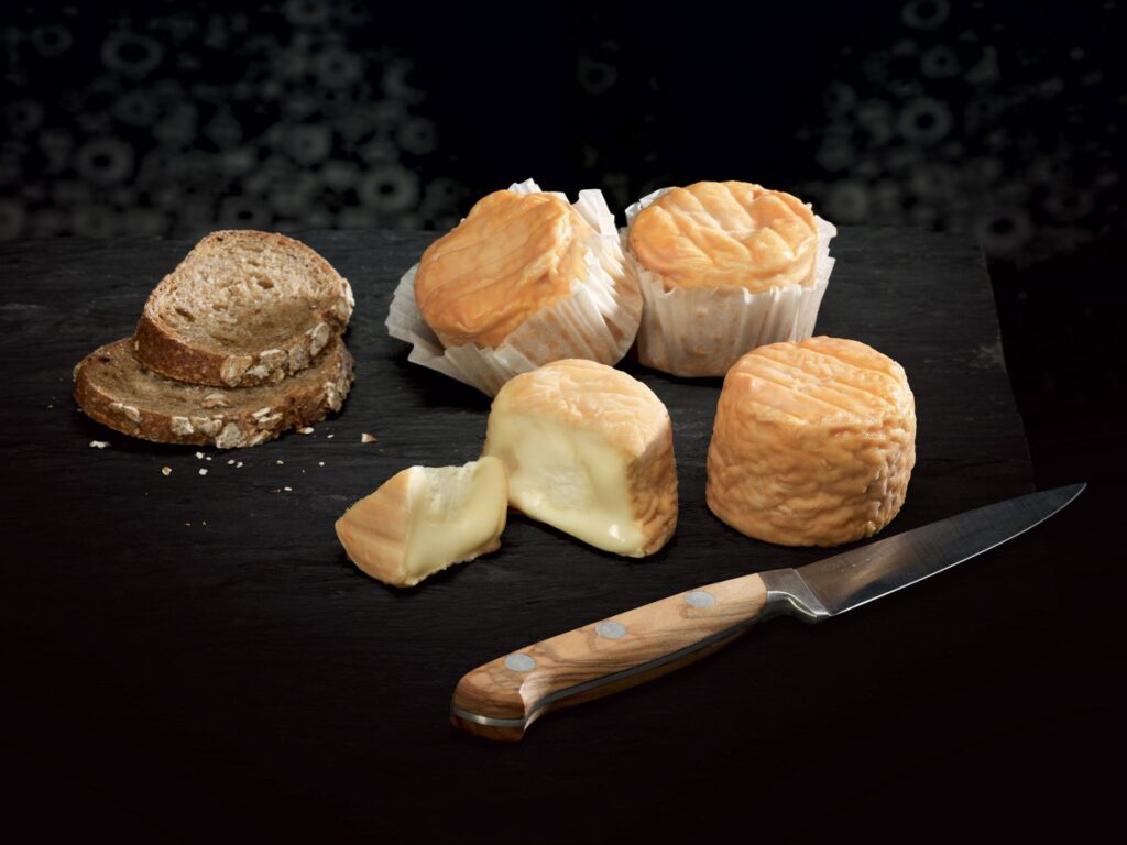 Small round and orange Trou du Cru cheeses on a dark wooden board