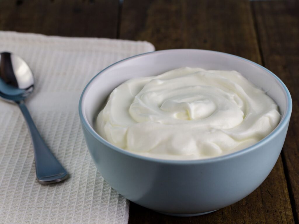 Bowl of Greek Yoghurt on a wooden table next to tablespoon