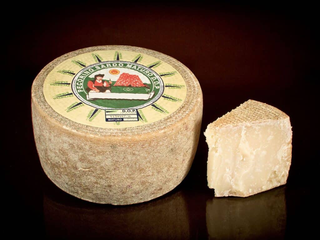 Wheel of Pecorino Sardo hard cheese next to cut wedge on black surface