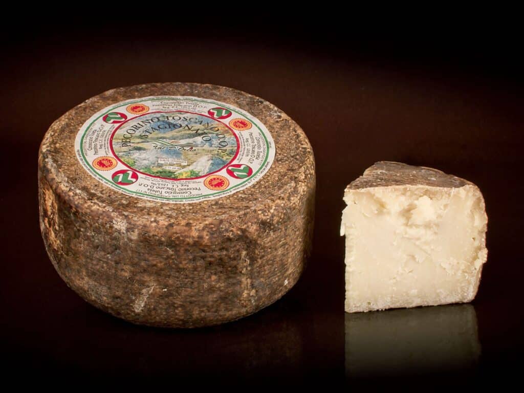 Wheel of aged Pecorino Toscano cheese on dark surface