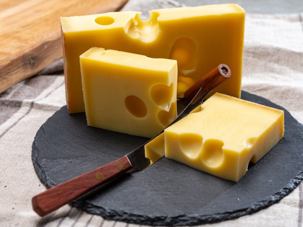3 pieces of Emmentaler cheese with large holes on a slate board