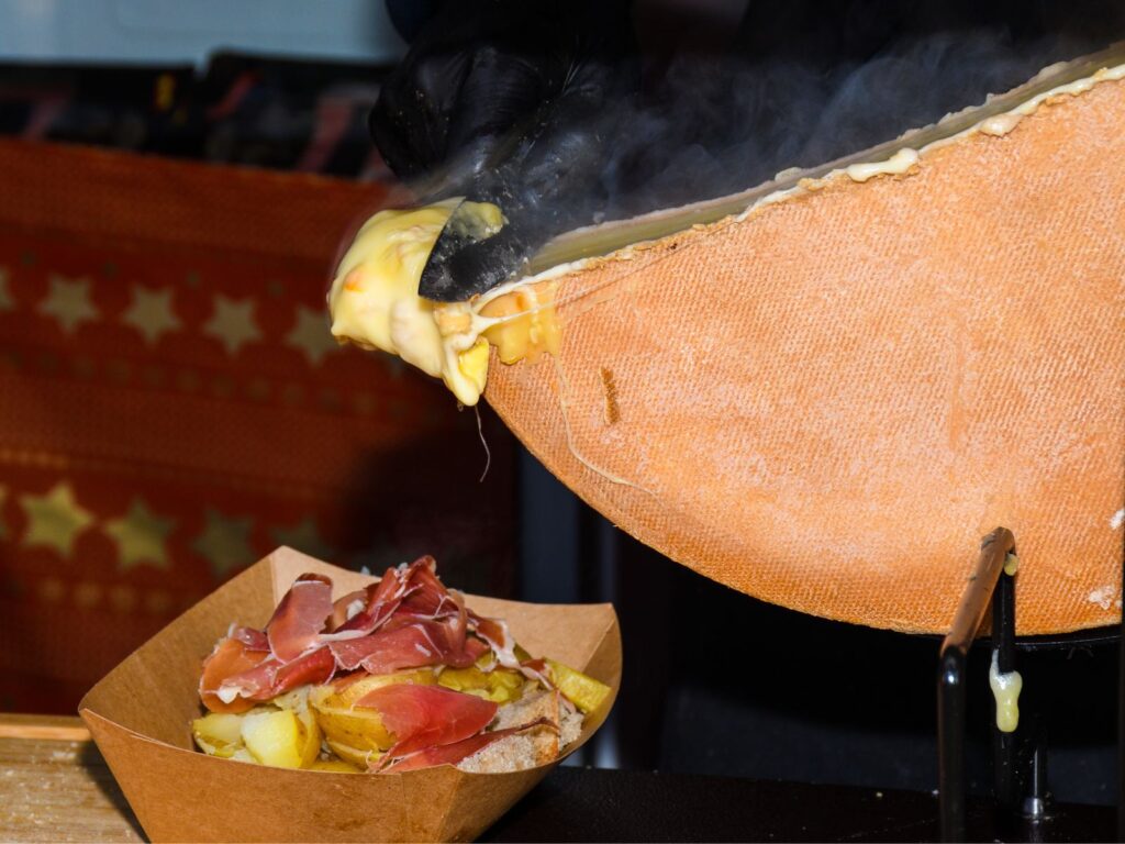 Wheel of melted Raclette scraped onto potatoes (Iconic Swiss cheese dishes)