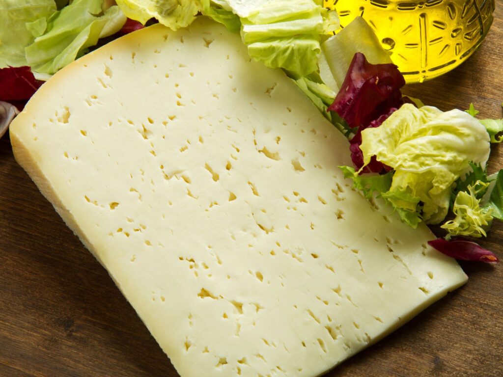 Young semi-firm cheese Asiago on a wooden board with fresh salad
