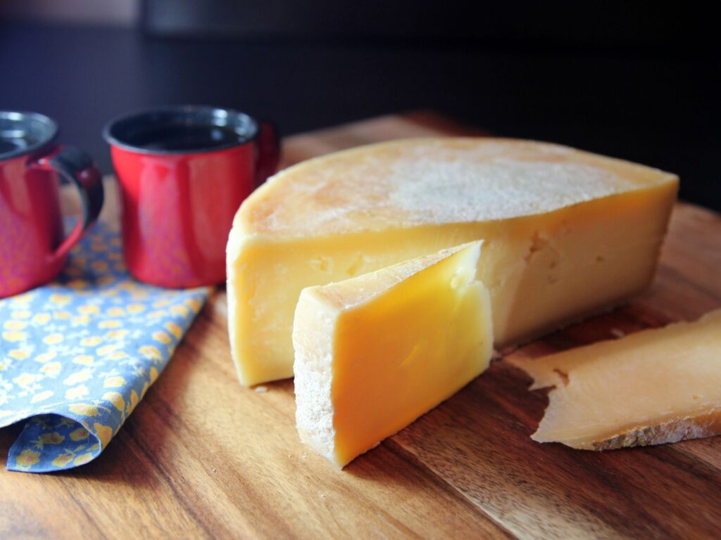 Half wheel of Canastra cheese on a wooden board next to cup of black coffee