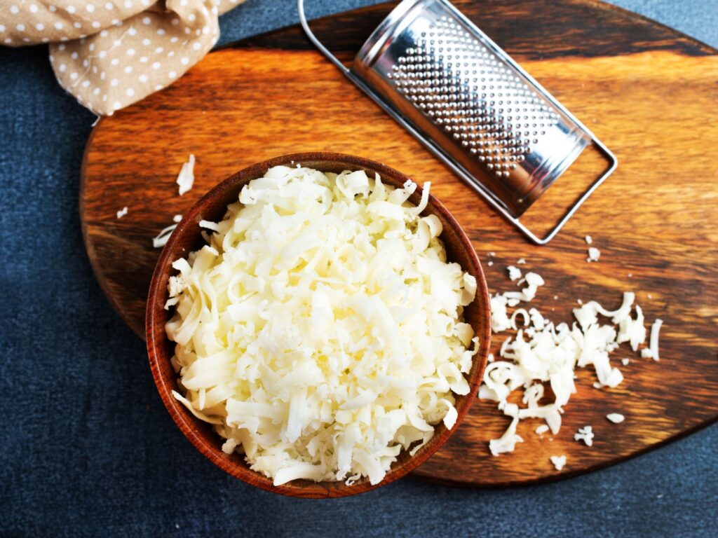 Shredded White Cheddar in a brown bowl on a wooden board