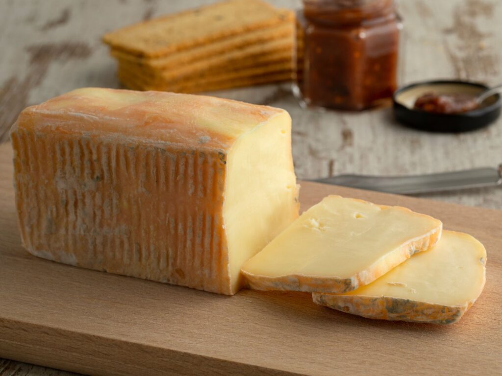 Brick of Taleggio Italian washed rind semi-soft cheese sliced on wooden board