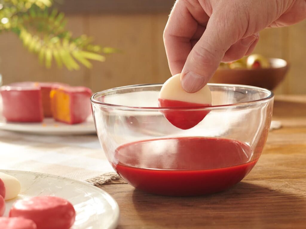 Woman dipping small round cheese in melted red wax to coat